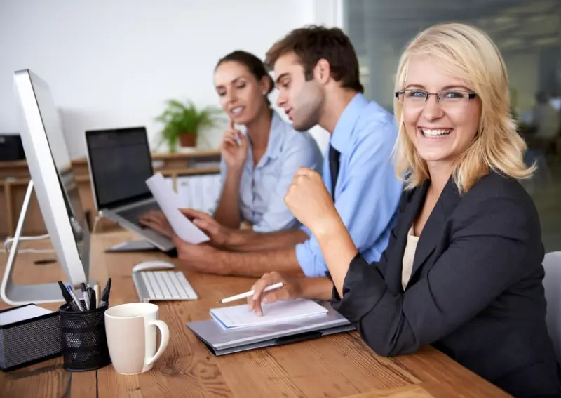 Smiling businesswoman works with team at computers adding company info to the directory to reach more local customers